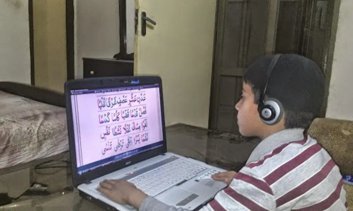 Child in yellow shirt looking at Quran on a laptop screen
